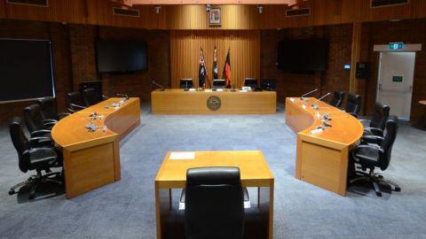 The empty Council Chambers - desks in a circle facing each other with empty seats.