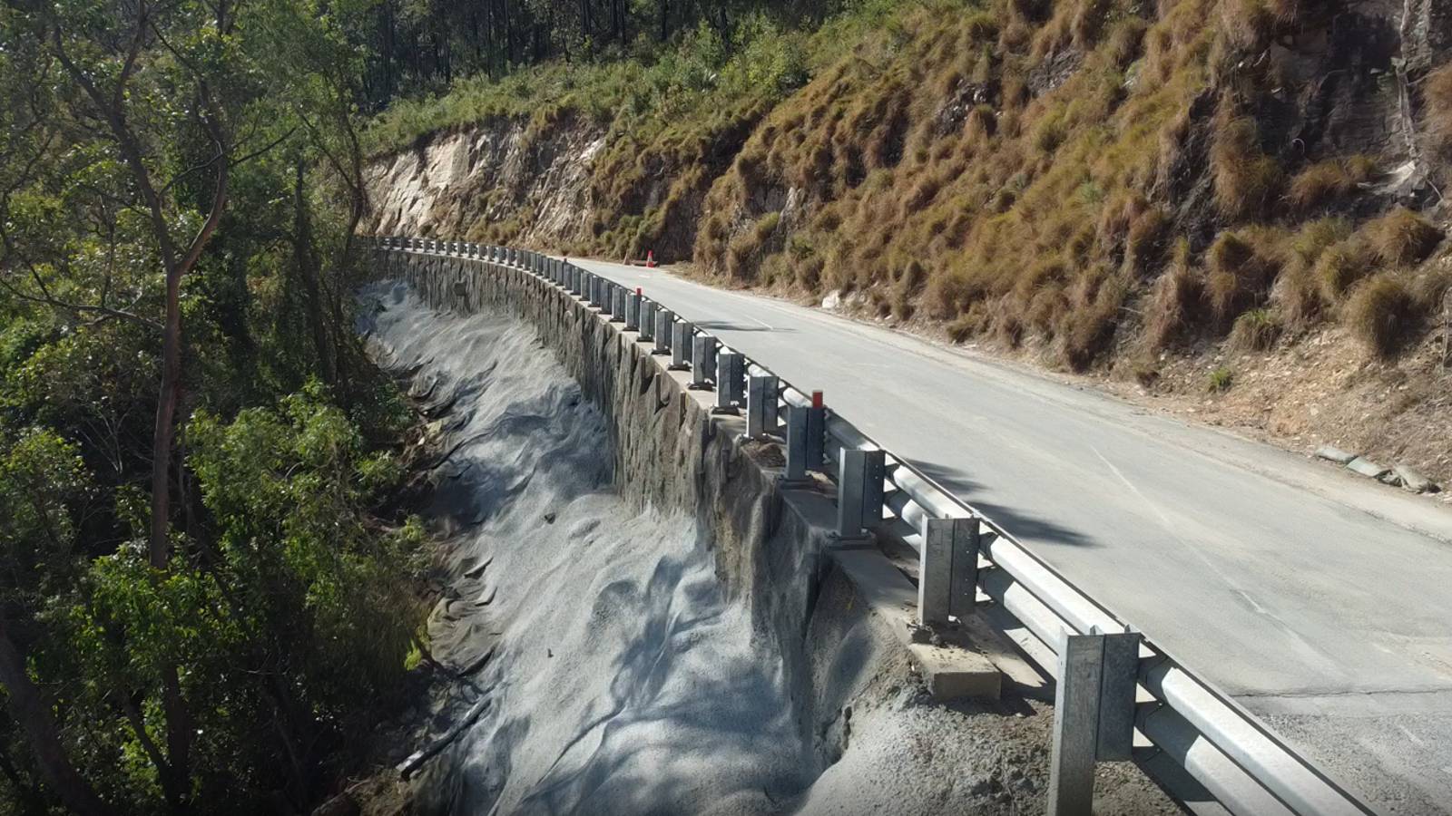 Concrete lines the steep roadside bank beneath a road lined with guardrail