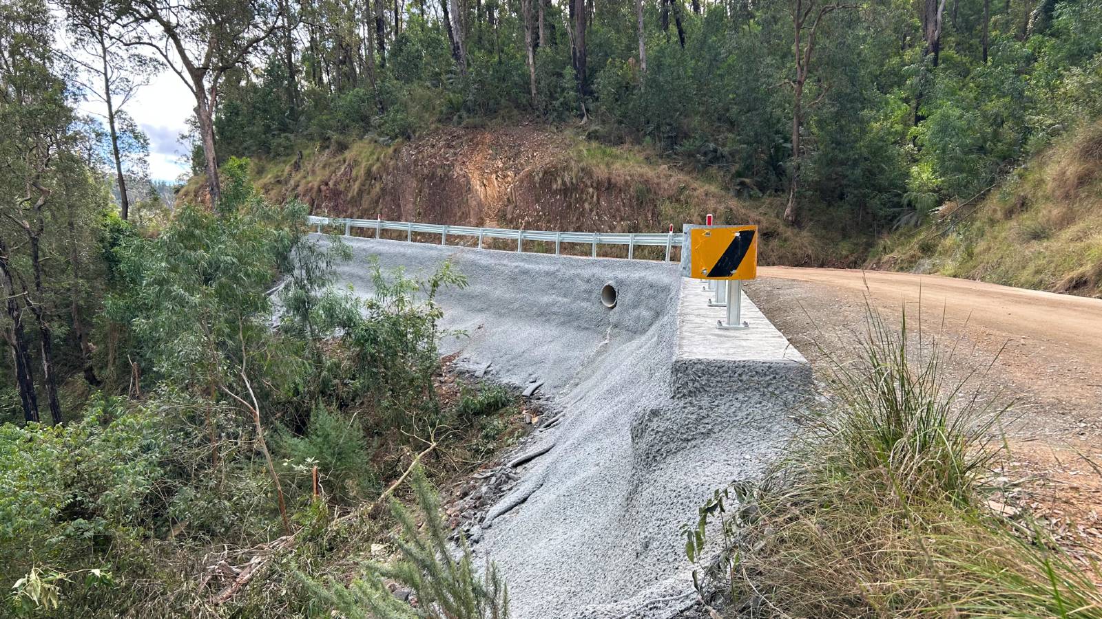 Image Concrete lines the steep bank of a dirt roadside in a bush setting.