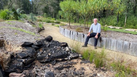Man with grey beard sitting in partially burnt landscaped garden