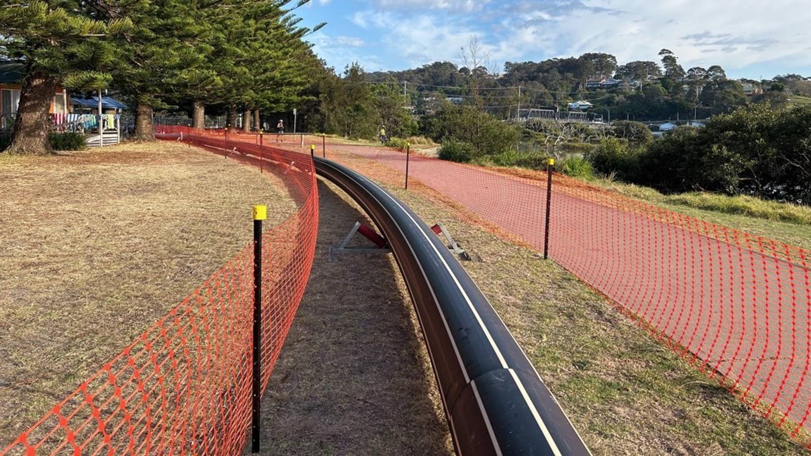 A large long black pipe is laid out along a grassed area with bunting on either side