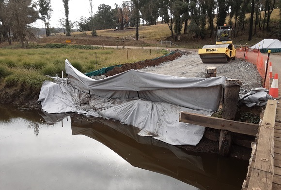 Image Geotech fabric lines the edge of the creek while a roller compacts road base on the approach for the new bridge