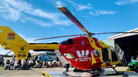 Crouching bystanders near a Westpac helicopter.