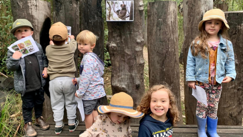 Children standing on a log smiling 