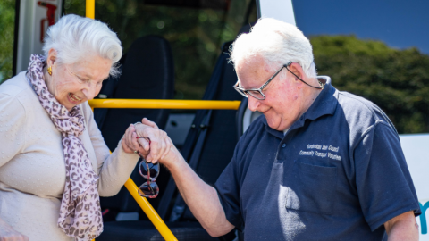 Elderly woman holds man's hand while exiting vehicle 