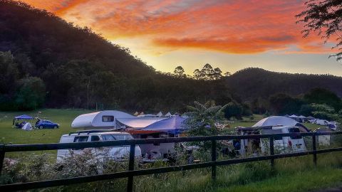 caravans and tents behind a fence with an orange sunset.