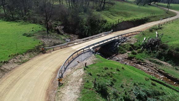 Image A single span bridge crosses a creek amid green paddocks