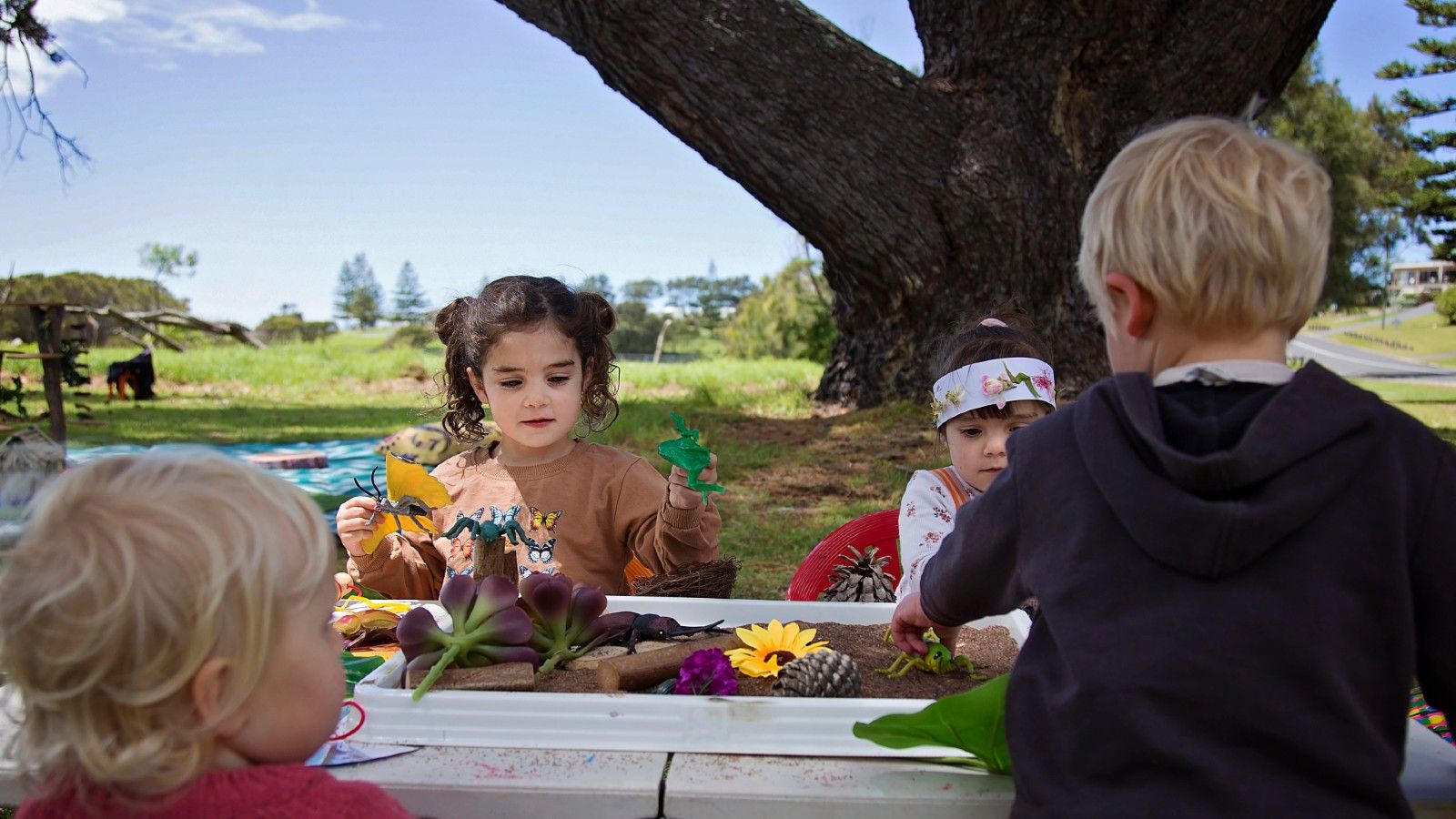 Four young children playing and creating with items in sandbox. banner image