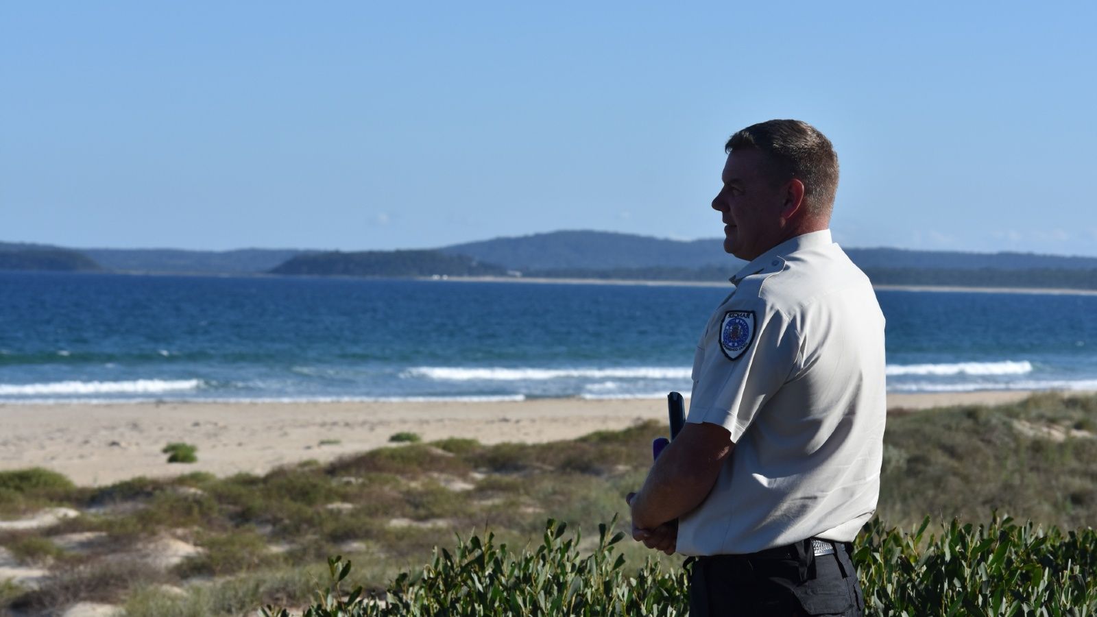 Close up image of a Ranger in uniform standing on the beach looking out at the ocean banner image