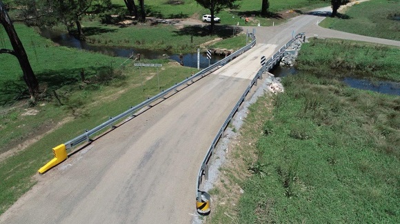 Image An aerial image shows a bridge lined with guardrail crossing a creek in a grassy area.