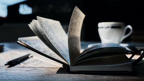 A hand-written journal open on a desk, next to a cup and a pen.