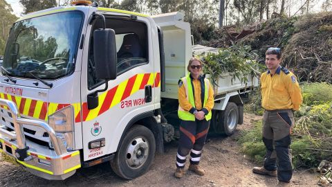 Woman and man in fire fighting clothes by truck holding tree clippings