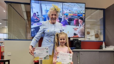 Smiling older woman and child proudly displaying certificates.